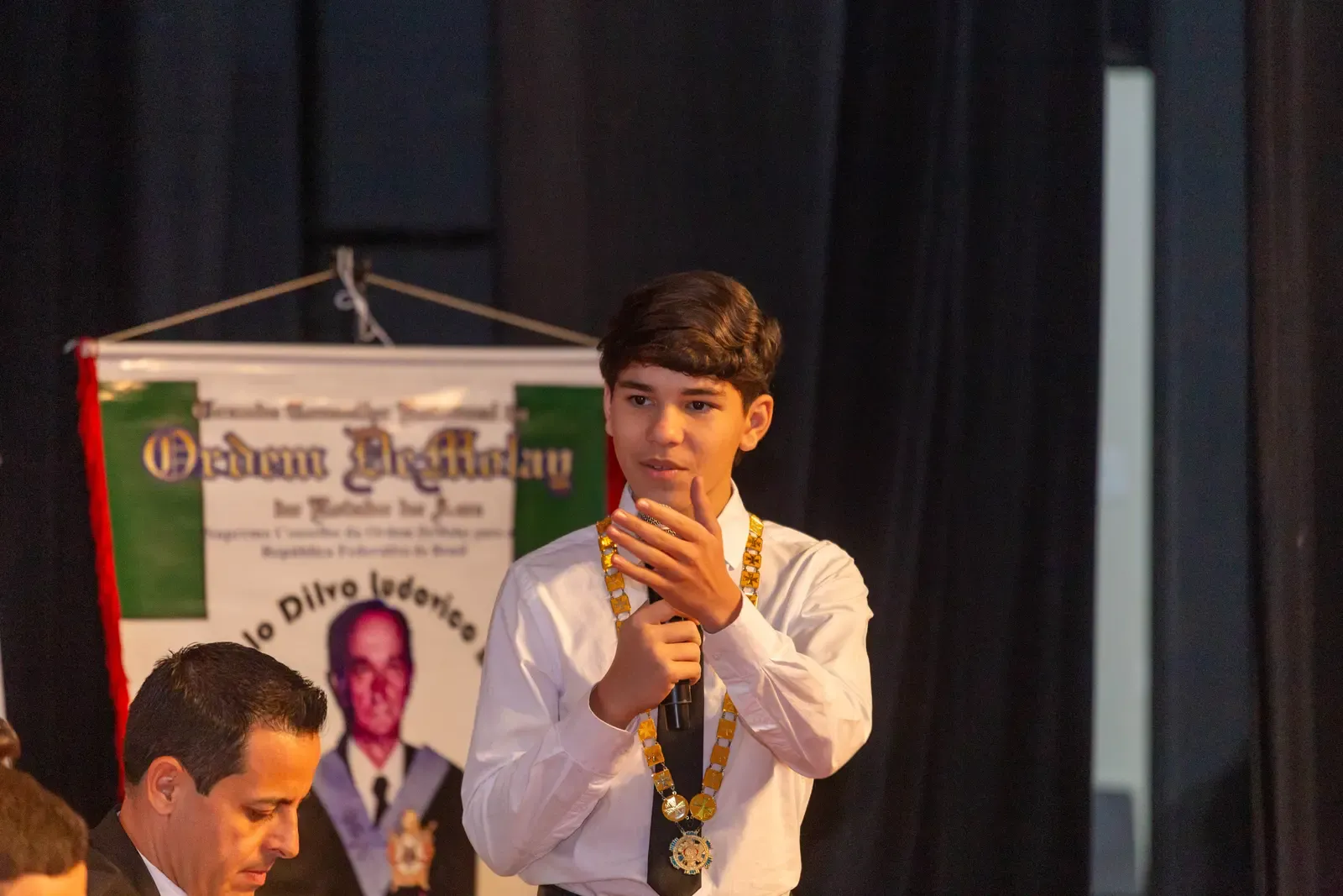 Jovem discursa ao microfone em um evento da Ordem