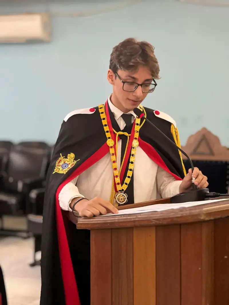 Jovem DeMolay de capa cerimonial discursa em uma tribuna de madeira
